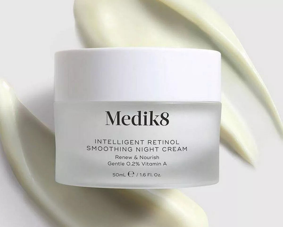 A white cylindrical container labeled "Medik8" with the brand name prominently displayed, positioned on a textured, light-colored background. The product is presented in a cream or lotion form, designed for skincare purposes.