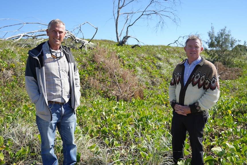 Two men stand in sand dunes looking at camera