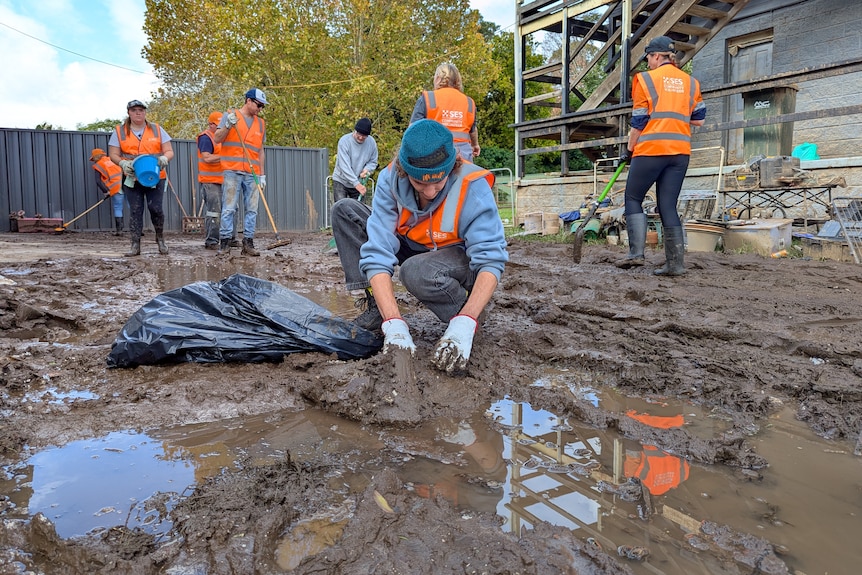 People in high-vis clear mud from a yard near a house.
