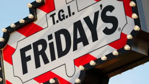 PA Media A TGI Friday's sign, with the font in black surrounded by white and red stripes and light bulbs. 