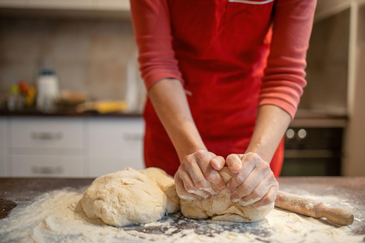 Woman preparing and kneading dough for bread and cakes. She wears a red apron and works in her kitchen. She is unrecognizable