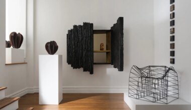 Modern art gallery featuring abstract sculptures and geometric installations in a minimalistic white room with wooden flooring.