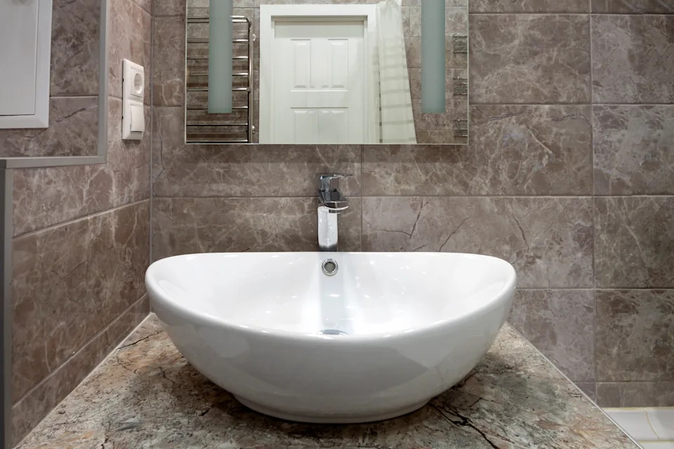 A modern bathroom sink with a round white basin and a sleek faucet, set against a marble wall and countertop