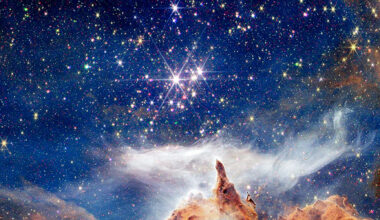 A winter scene fit for a holiday greeting card. Above what appears to be a fantastical snowy mountainscape, is a brilliant blue sky packed with colorful lights. The golden mountainscape is in fact part of the nebula NGC 6357, as captured by NASA's James Webb Space Telescope. The green, red, and golden lights in the blue sky above are bursts of high-energy X-rays from active stars, detected by Chandra.