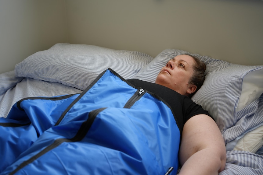 A woman laying in bed wearing a blue medical suit.