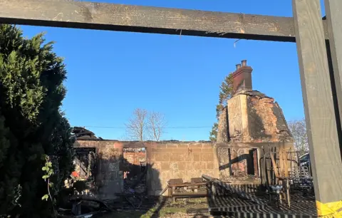 The shell of a house after a fire, with just parts of the walls still standing. It is a clear day
