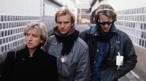 Getty Images Andy Summers, Sting and Stewart Copeland in an alleyway in Japan in 1981 - they are wearing winter clothing, jackets and scarfs. Sting is the only one looking at the camera