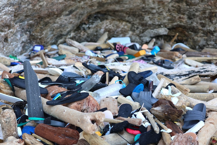 A massive pile of plastic debris on a beach, including rubber thongs, slip-ons and other shoes.