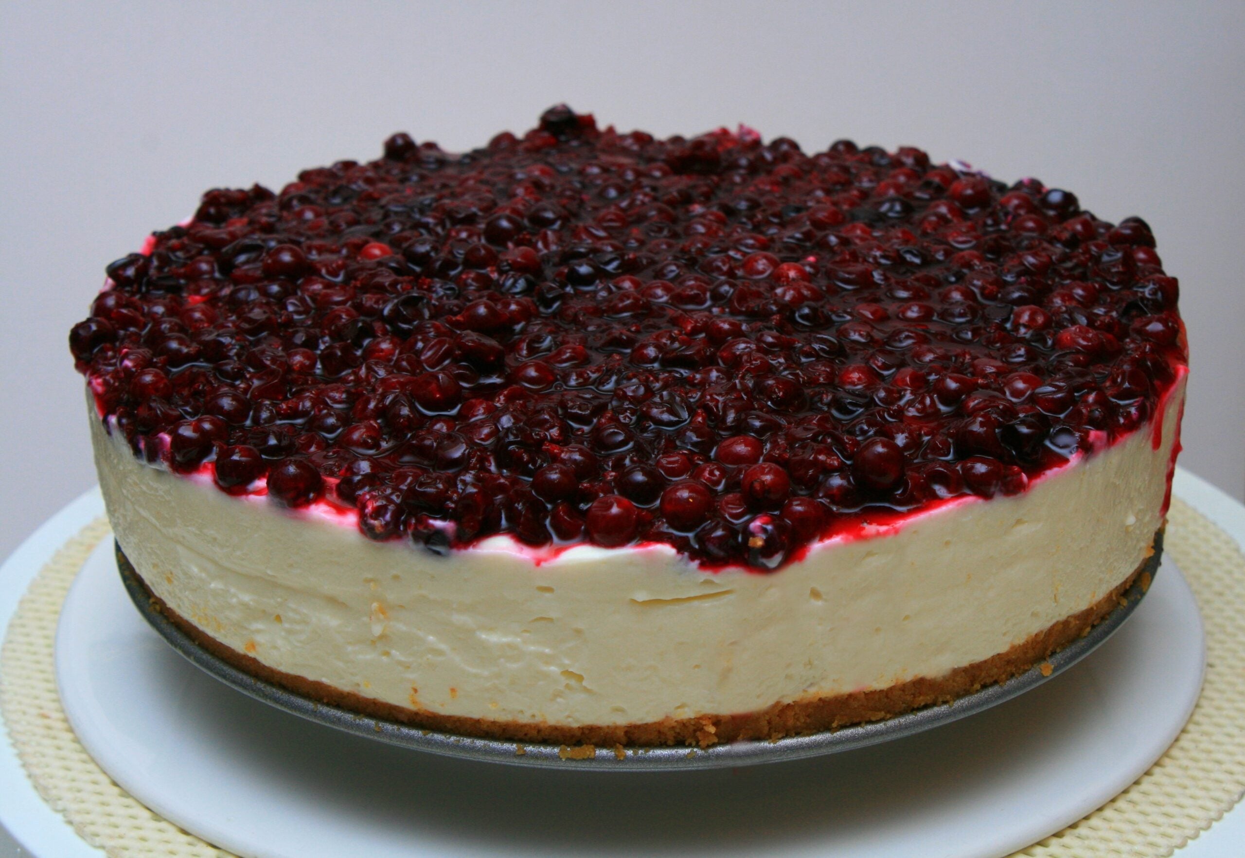 A cheesecake topped with a layer of mixed berries on a graham cracker crust, displayed on a white plate.