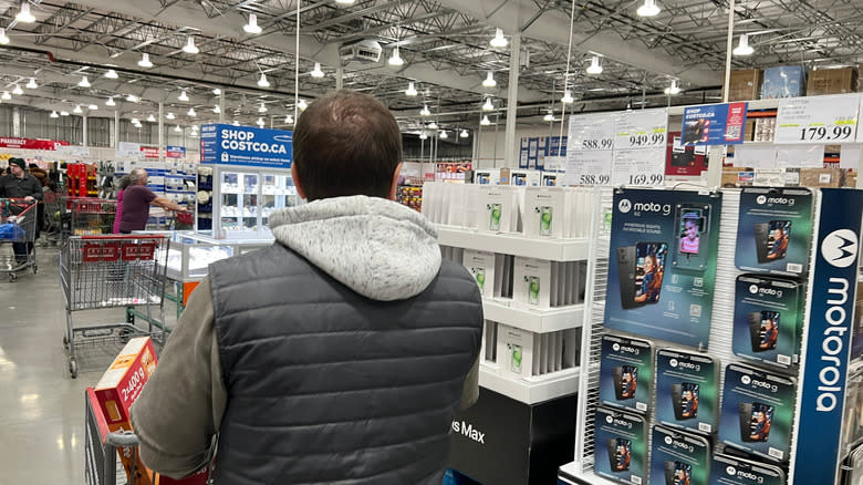 A man walking past a smartphone display at Costco.