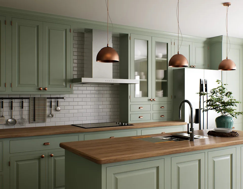 Modern kitchen with green cabinets, wooden countertops, copper pendant lights, and a central island. A potted plant sits on the island