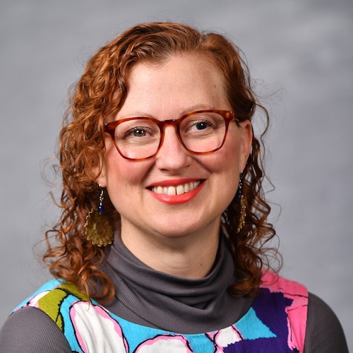 Smiling woman with long curly hair and eyeglasses.