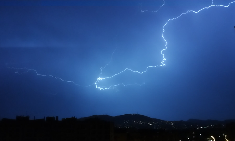 A dark sky with blue shades and long, glowing jagged line streaking across it but not touching the ground.