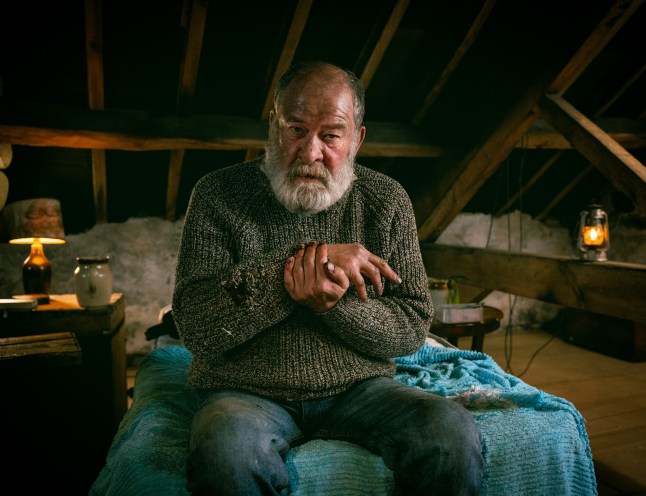 Bear Wolf looking distressed while trapped in a barn in Emmerdale. He is holding his injured hand and wrist.