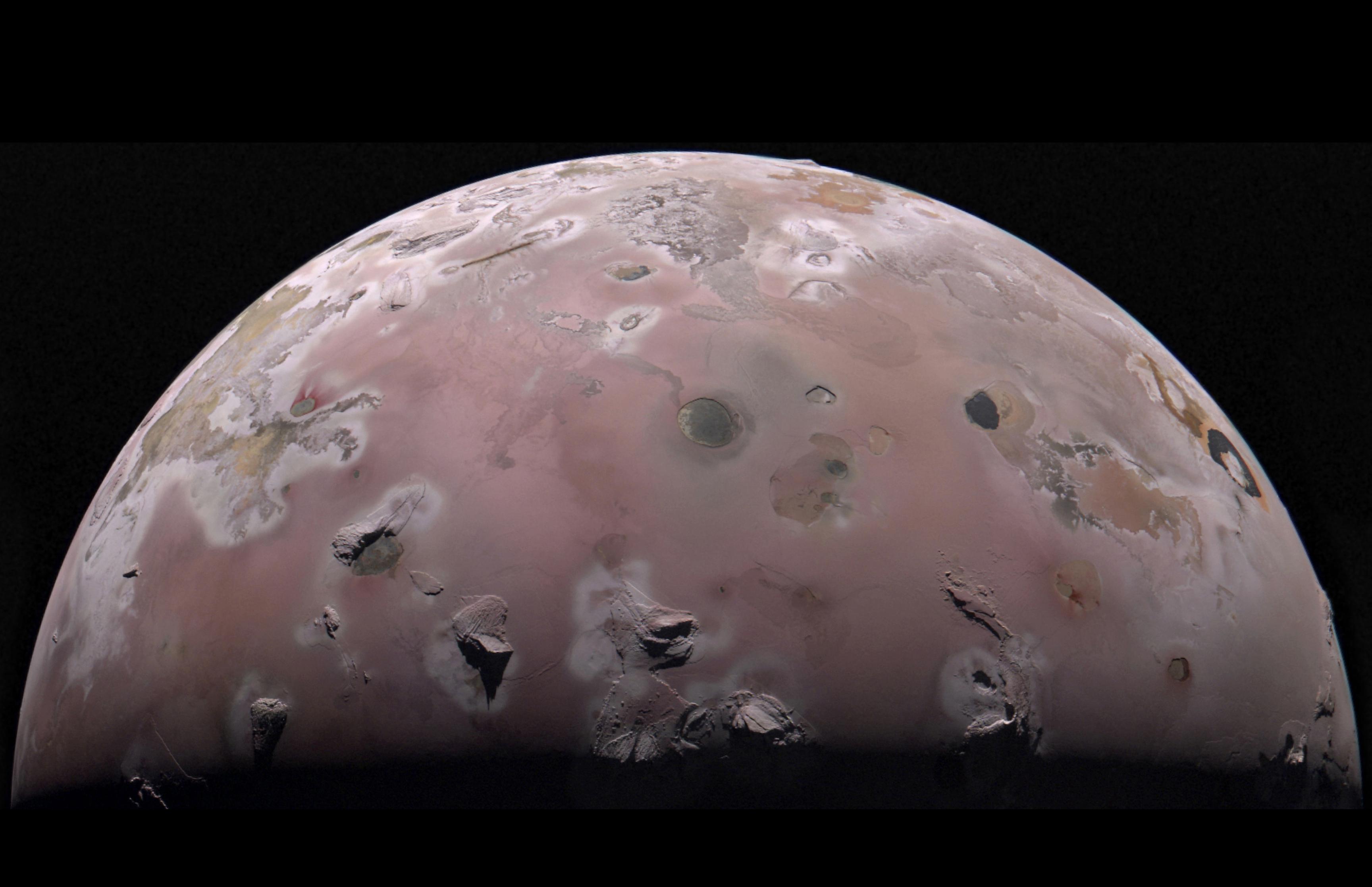A close up of the planet Io, its pinkish surface dotted with dark spots and ridges