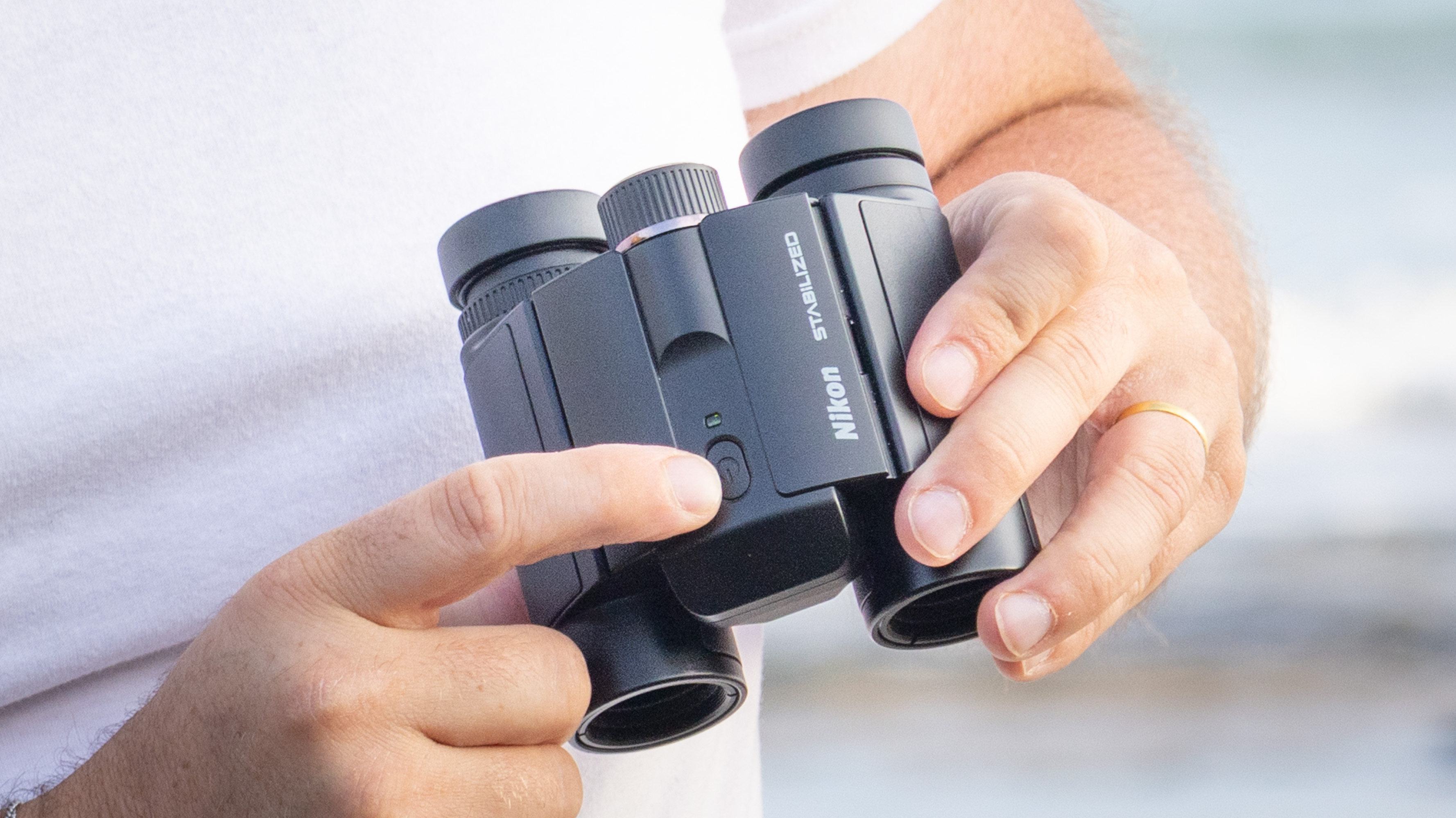 Nikon Stabilized 12x25 S binoculars held in the hands of the reviewer in front of breaking waves at the beach