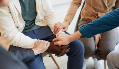 Image depicts a small group of four people holding someone's hands to show support.