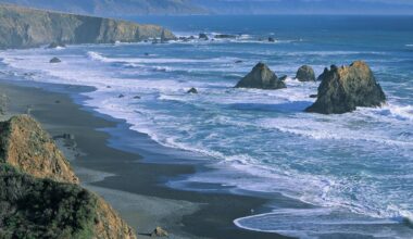 View of rocky coastline and beach to left with island rocks among the surf to right.