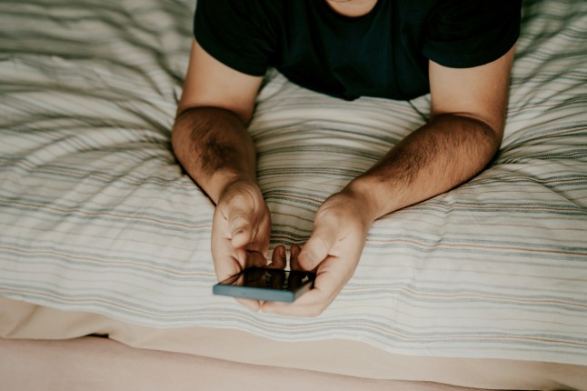 Person using smartphone while relaxing on a comfortable striped bed