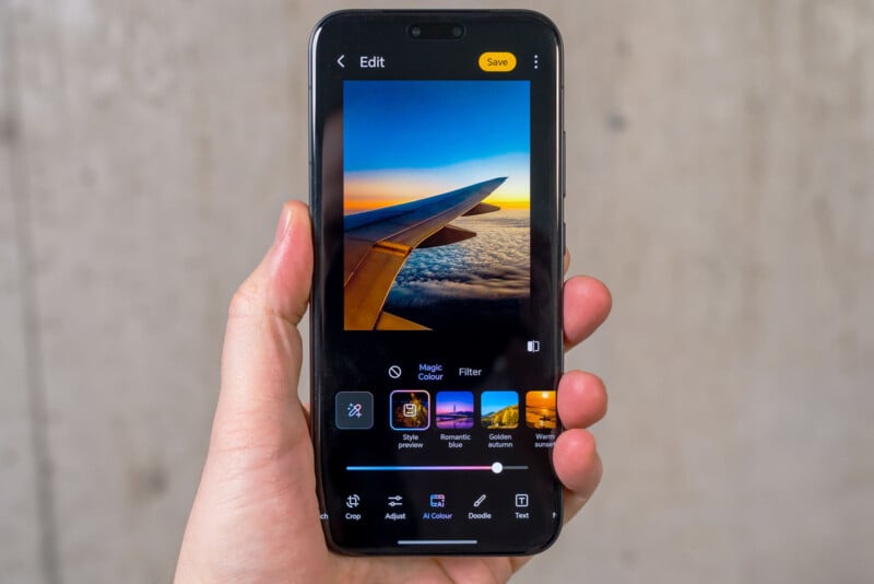 A hand holds a smartphone displaying a photo editing app. The screen shows a photo of an airplane wing above clouds at sunset, with editing options and filters visible below the image.