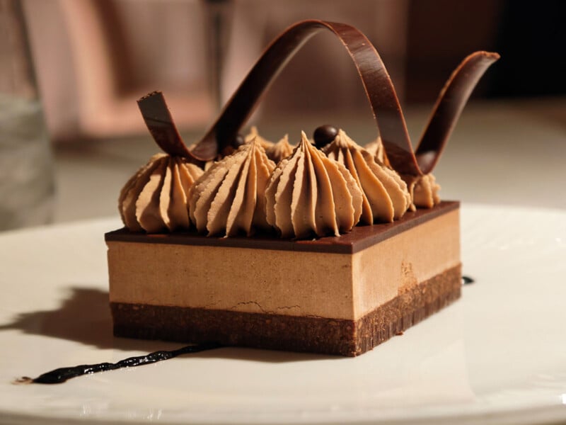 A gourmet chocolate mousse dessert topped with decorative chocolate swirls and piped cream, served on a white plate with a drizzle of chocolate sauce.