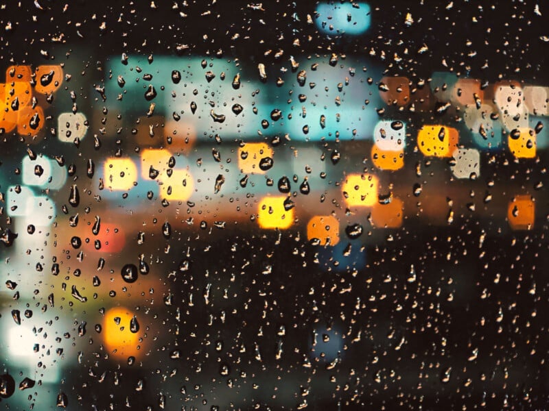 Raindrops on a window with blurred city lights in the background at night, creating a bokeh effect.