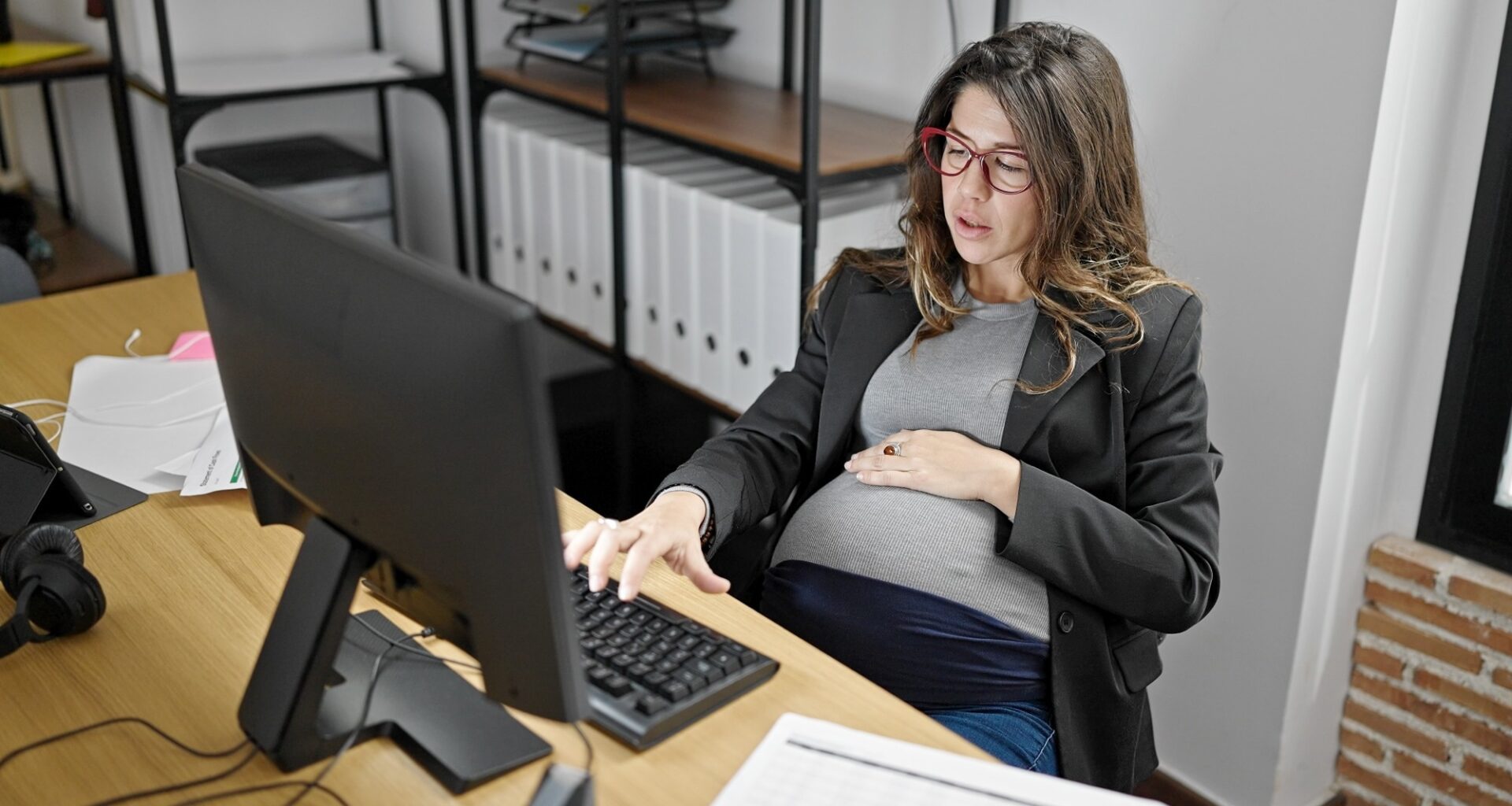 Young pregnant woman business worker using computer touching belly at office