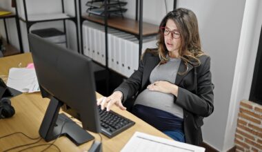Young pregnant woman business worker using computer touching belly at office