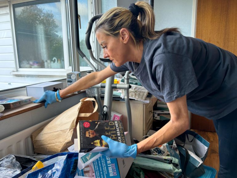 Jo Powell dons gloves as she sifts through a hoarder's belongings, carefully picking out important mementoes. [Amandas Ong/Al Jazeera]