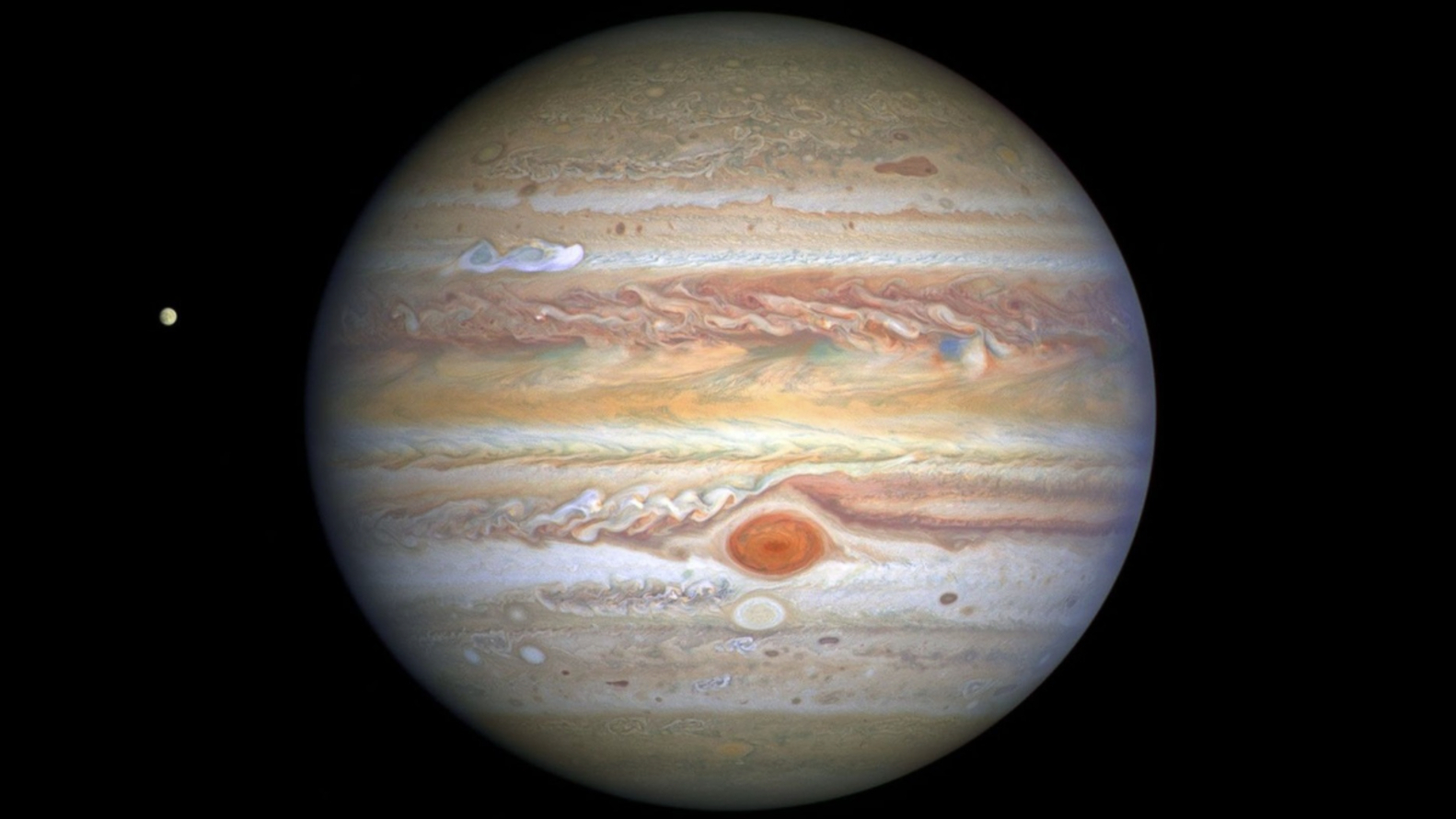 An image of Jupiter pictured against the blackness of space, with one of its moons appearing as a small sphere to its left.