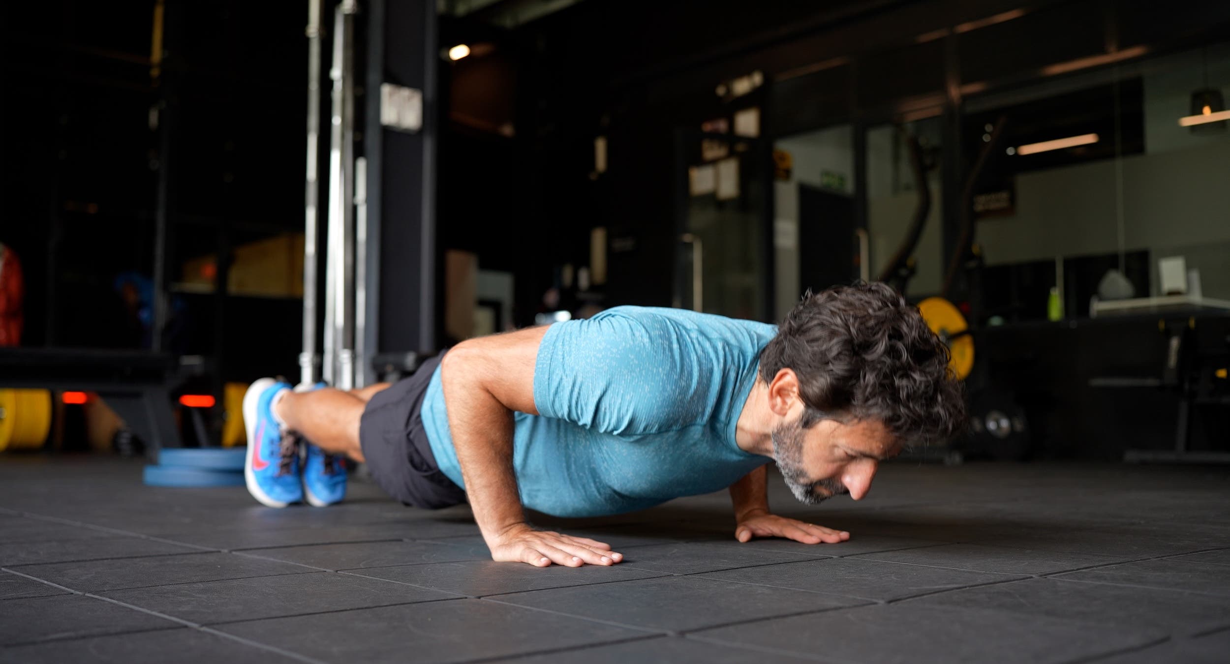 main with dark hair and a beard does a push-up on the floor at a gym as part of a longevity workout plan