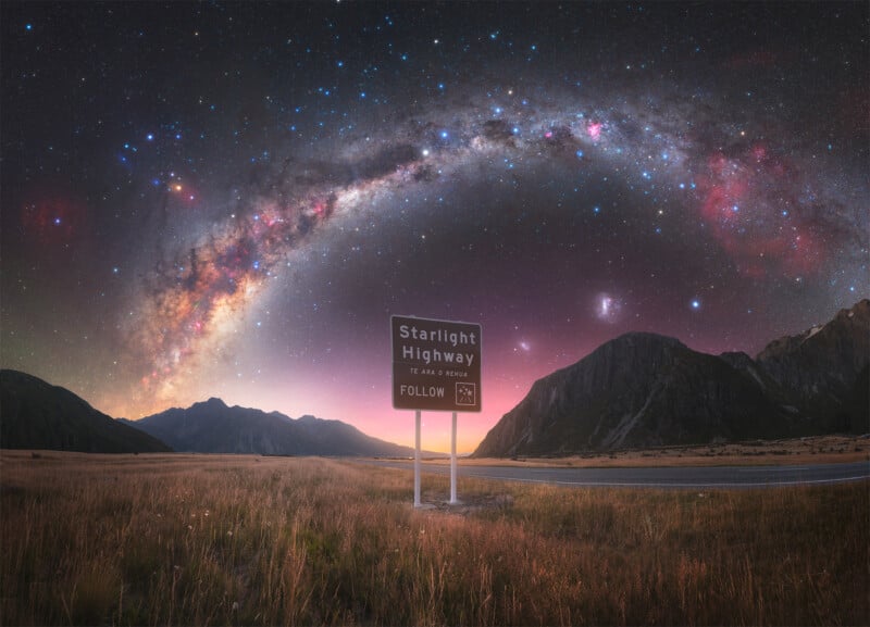 A road sign reading "Starlight Highway" stands in a grassy field with mountains in the background. Above, a vivid, colorful Milky Way arc stretches across a star-filled night sky.