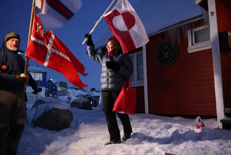 Aviaq Brandt (44) holds a Greenlandic flag as she stands with Jens Kjeldsen (70), holding a staff adorned with the flags of the three territories of the Kingdom of Denmark, outside the US consulate in Nuuk, Greenland. Photograph: Sean Gallup/Getty Images
