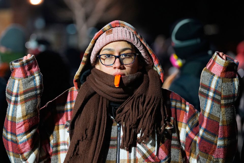 A person holds a whistle in their mouth as police face off with protesters during a noise demonstration outside the Graduate by Hilton Minneapolis hotel on Wednesday, Jan. 28, 2026, in Minneapolis. (AP Photo/Adam Gray)