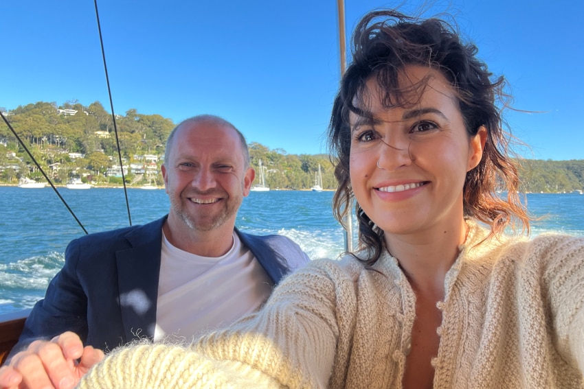 Yasmine, right, beams while wearing a beige knit cardigan with Anthony behind her, left, on a boat together.