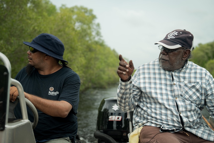 Two people on a tinny as it travels through wetlands.