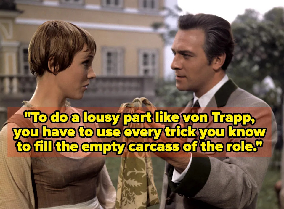 Two people in period costume are in conversation; one is holding a patterned cloth. An older building is in the background