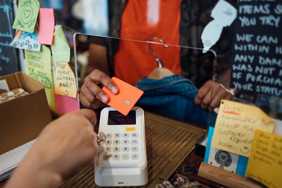 An unrecognisable young man enjoying a day out shopping in a vintage clothing store in Durham, North East England. He is paying via contactless for his purchase at the till with a credit card on a credit card reader.