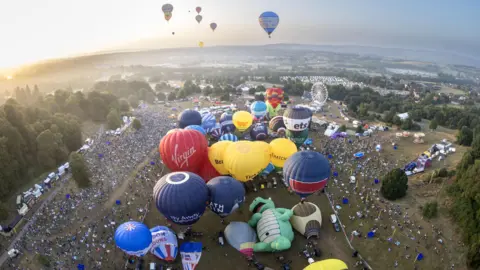 Bristol International Balloon Fiesta Hot air balloons in the air above Bristol in a picture taken from another balloon. The balloons are a variety of colours and the parkland of Ashton Court is visible beneath them along with large crowds