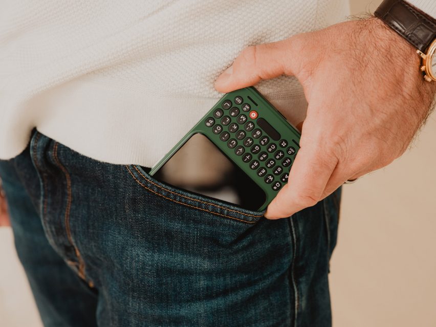 Close-up photo of a person's hand sliding a dark green Clicks Communicator phone into their jeans pocket