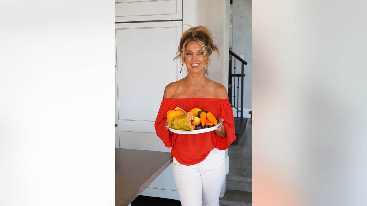 Denise Austin holds a fruit basket while smiling.