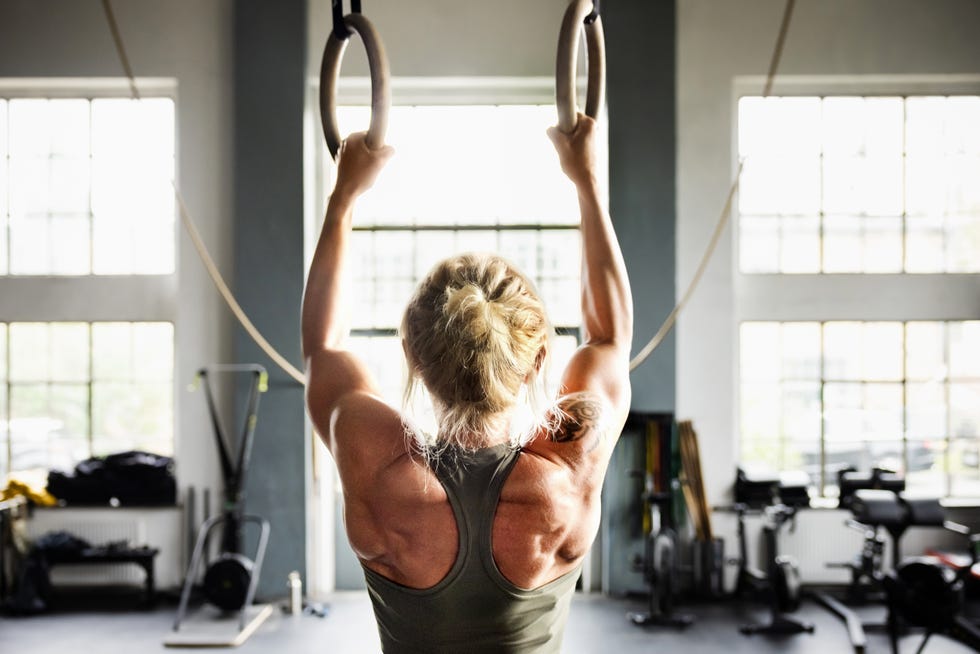 Determined female athlete working out on gymnastic rings during cross training session in modern light filled gym determined female athlete working out on gymnastic rings during cross training session in modern light filled gym