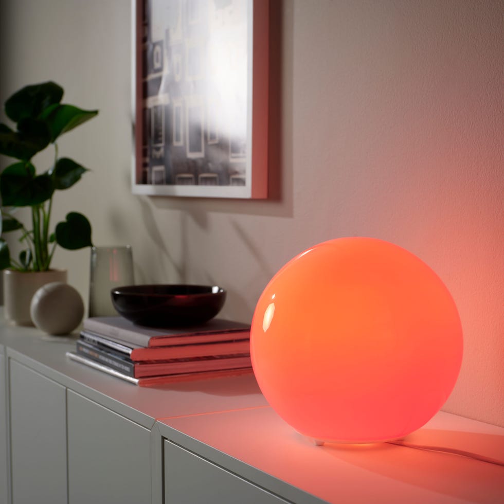 IKEA's KAJPLATS smart bulbs in a FADO lamp a glowing orange spherical lamp on a console table
