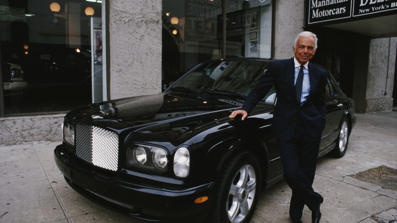 Ralph Lauren posing with a black Bentley at a showroom