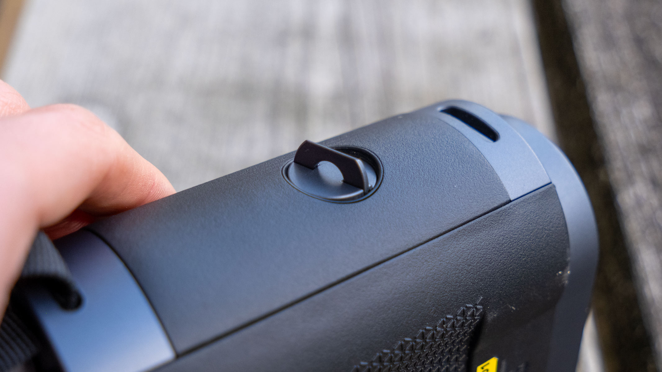 A close-up of the battery compartment on the Fujifilm Techno-Stabi TS-L 1640 image-stabilized binoculars with wooden slats in the background.