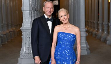 A man wearing a black suit and bowtie stands to the left of a woman in a sparkly blue dres.