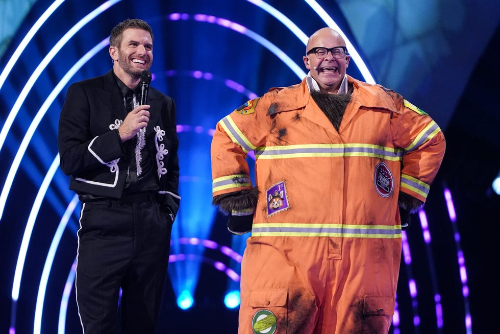 masked singer uk joel dommett harry hill red panda two individuals on stage one holding a microphone and the other in a firefighter costume