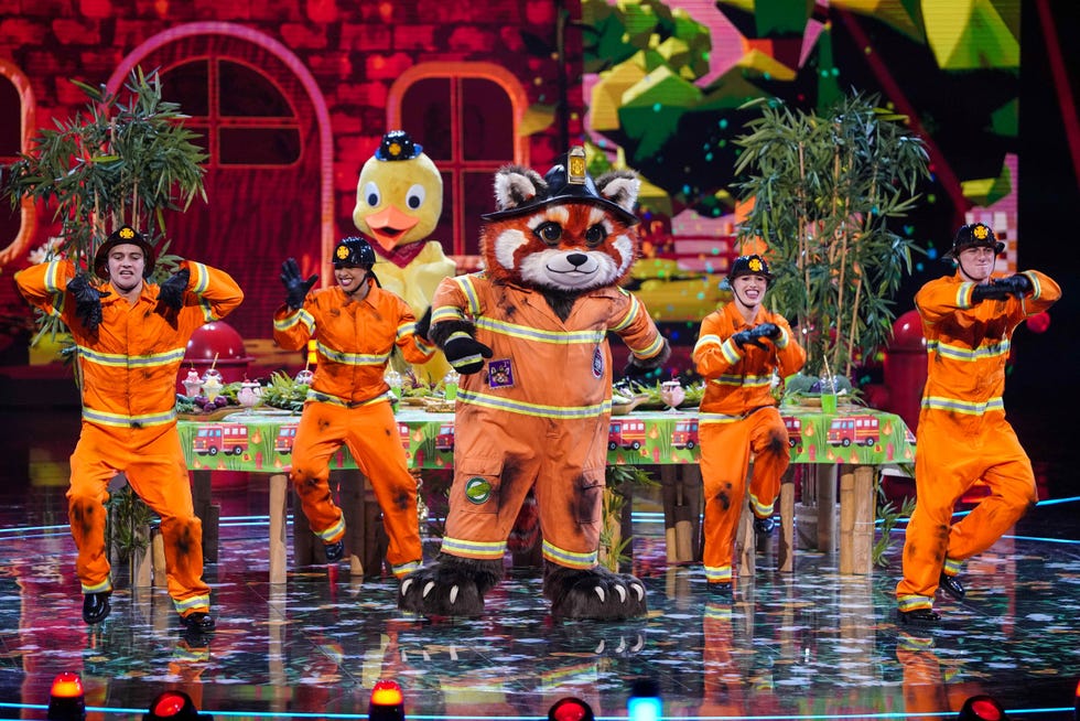 masked singer uk red panda performance featuring characters in mascot costumes and dancers in orange outfits
