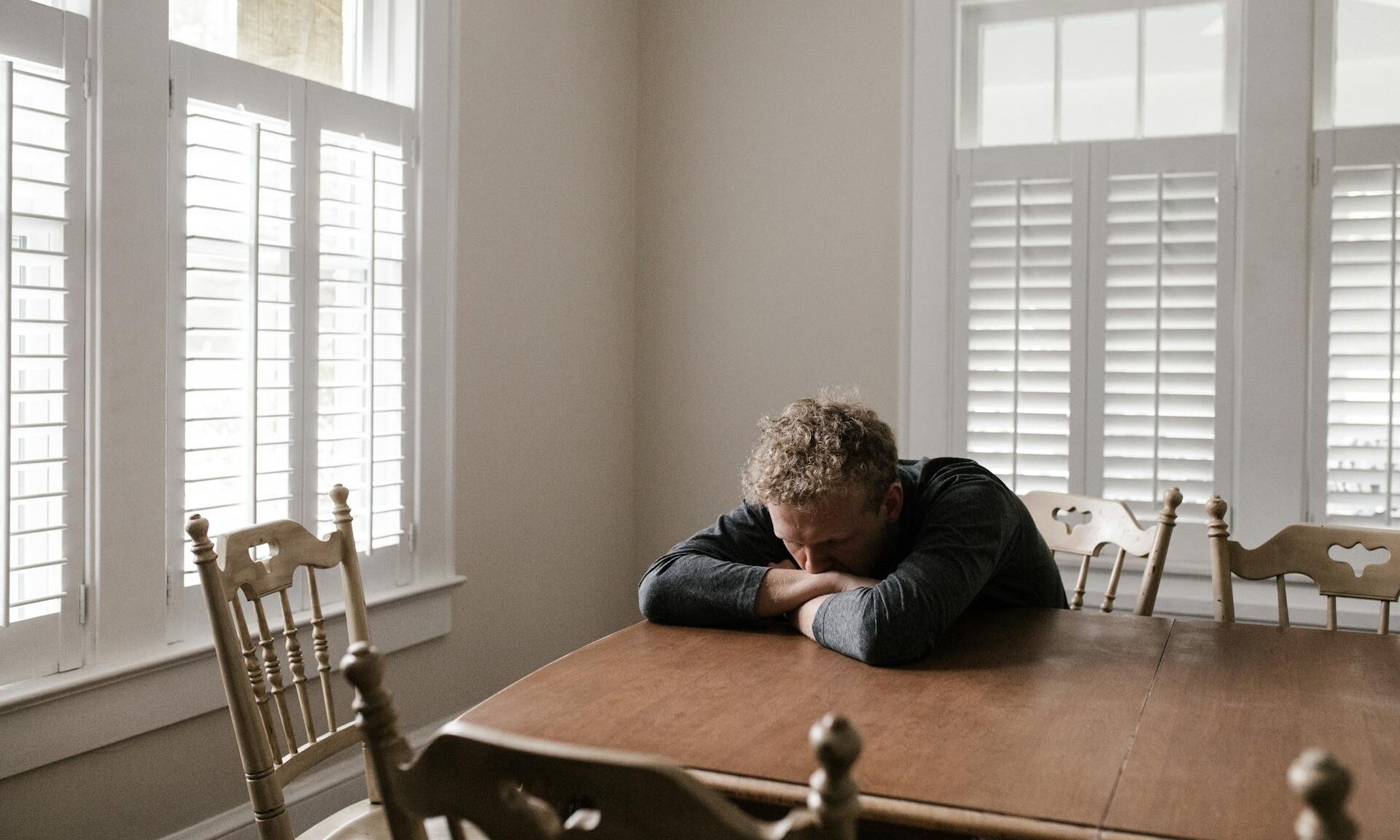 man resting head on table thinking down depressed