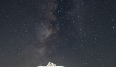 A white radio antenna faces upward in the direction of a star-studded night sky.